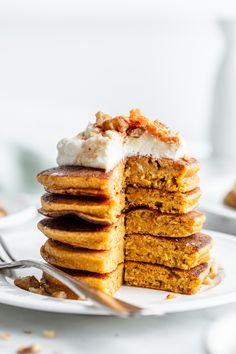 a stack of pancakes sitting on top of a white plate with whipped cream and walnuts