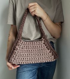 a woman is holding a crocheted purse in her left hand and wearing a gray t - shirt