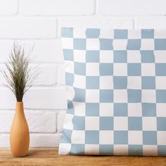 a blue and white checkered pillow sitting on top of a wooden table next to a vase