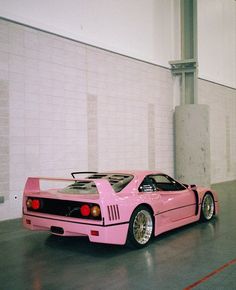 a pink sports car parked in a parking garage next to a white brick wall and floor