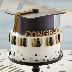 a graduation cake decorated with black and white icing, gold letters and tassels