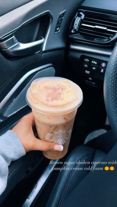 a person holding a cup of coffee in their hand while sitting in the driver's seat of a car