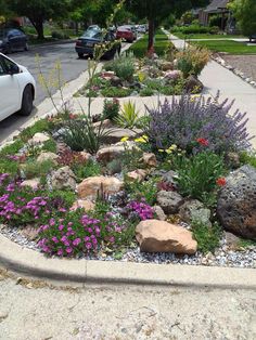 a white car parked on the side of a road next to a flower bed with rocks and flowers