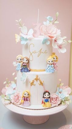 a three tiered cake with princess figurines on top and flowers around it