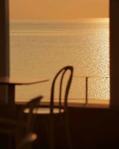 two chairs and a table in front of an open window overlooking the ocean at sunset