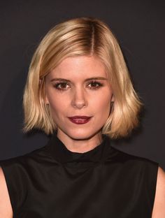 a woman with short blonde hair wearing a black dress and dark lipstick looks at the camera