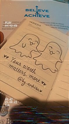 a hand holding a book with writing on it and two ghost faces drawn on the pages