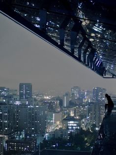 a person standing on top of a tall building at night with city lights in the background