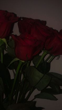 some red roses are in a vase with water on the bottom and green stems to the side