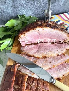 sliced ham sitting on top of a cutting board next to a knife and some greens