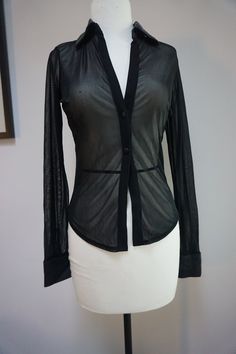 This blouse is from the 1990s, with a translucent material and an opaque collar, hemming, and buttons. The blouse is 100% polyester, but the collar and cuffs have a silky finish and feel. PLEASE NOTE: The line across the bottom-half of the blouse, which is visible in the photos, is NOT a feature of the blouse; it was part of the dress form and just showed up because of the blouse's translucent material. Size: Small Measurements when lying flat: Shoulders: 14 inches  Sleeve Length: 24 inches Sleeve Width: 5 inches Blouse Length: 20 inches Formal Tops With Sheer Sleeves And Stretch, Evening Collared Tops With Button Closure, Classic Sheer Tops For Formal Occasions, Classic Sheer Top For Formal Occasions, Formal Sheer Stretch Tops, Classic Sheer Blouse For Office, Classic Sheer Blouse For Work, Classic Sheer Tops For Fall, Long Sleeve Mesh Top For Work