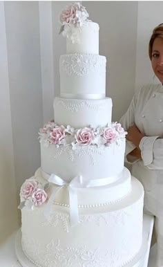 a woman standing next to a large white cake with pink flowers on it's side