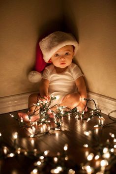 a baby is sitting on the floor surrounded by christmas lights with a santa hat on