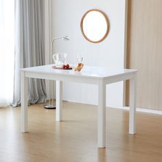 a white table with two glasses on it in front of a curtained window and a round mirror