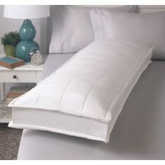 a white bed with pillows on top of it and a night stand in the background