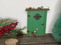 a green door is surrounded by red berries and greenery on a wooden table next to a christmas tree