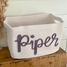 a crocheted basket with the word piper written in purple on it sitting on a wooden shelf