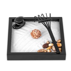 a tray with rocks, sand and black utensils in it on a white background