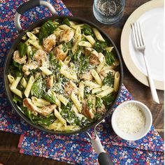 a skillet filled with pasta and chicken on top of a colorful place mat next to silverware