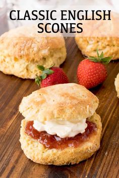 biscuits with jam and cream on top are sitting on a cutting board next to strawberries