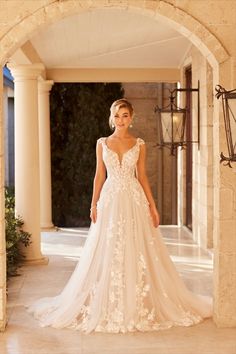 a woman in a wedding dress is standing under an archway with her hand on her hip