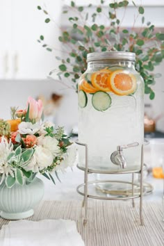 a jar filled with water sitting on top of a table next to a vase full of flowers