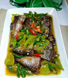 fish with peppers and green beans on a white square plate, ready to be eaten