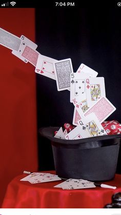 playing cards fall into a black bucket on a red tablecloth with flowers in the background