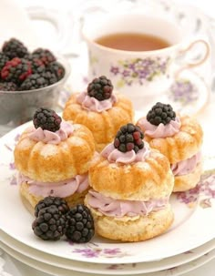 small pastries on a plate with blackberries and raspberries next to a cup of tea