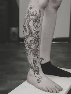 a person with a dragon tattoo on their leg sitting on top of a white object