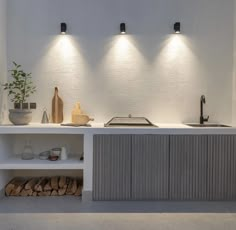 a kitchen with three lights above the sink and wood stacked on the counter top next to it