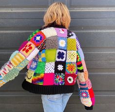 a woman wearing a multicolored jacket and jeans is standing in front of a garage door