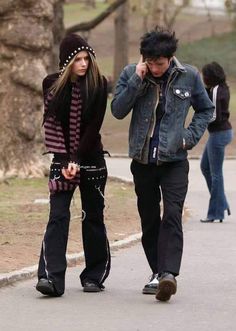 two people walking down the street talking on their cell phones while one person is holding his ear