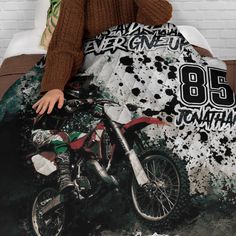 a woman sitting on top of a bed next to a dirt bike covered in black and white paint