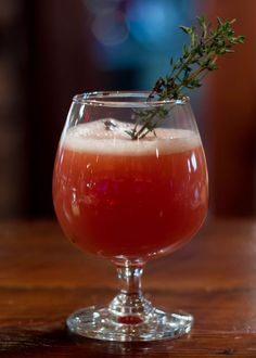 a glass filled with liquid and topped with a sprig of thyerole