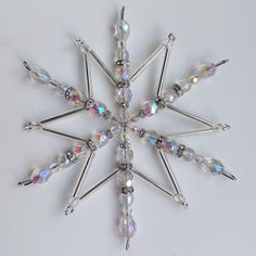 a snowflake made out of glass beads and silver pins on a white surface