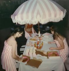 three women sitting at a table with food under an umbrella in front of their faces