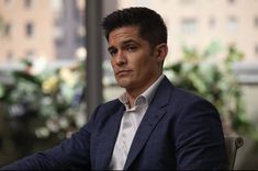 a man in a suit sitting at a table with his hands on his knees and looking off into the distance