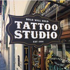 a tattoo studio sign hanging from the side of a building