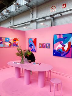 a pink room with paintings on the wall and a woman sitting at a round table