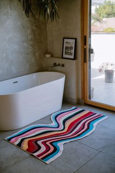 a bath tub sitting next to a window in a bathroom with a rug on the floor