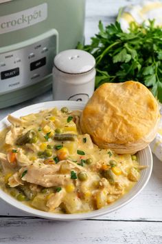 a bowl of chicken pot pie soup next to an open crockpot on a white table