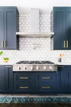 a kitchen with dark blue cabinets and gold pulls on the stove top, along with an area rug