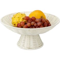 a white wicker fruit bowl with grapes, orange and pineapple in it on a white background