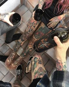 two people with tattoos on their legs are holding wine bottles and looking down at the floor