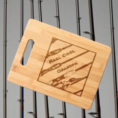 a bamboo cutting board with the words real cool grandpa on it and fishing rods in the background