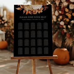 a black and white wedding seating chart on a easel in front of pumpkins