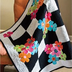 a black and white quilt with colorful flowers on the front, sitting on an orange chair