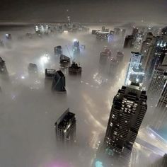 an aerial view of a city in the middle of foggy skies with skyscrapers lit up at night