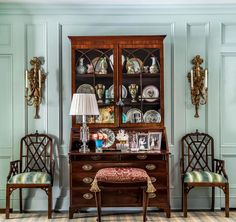 an old fashioned china cabinet with two chairs and a table in front of the hutch